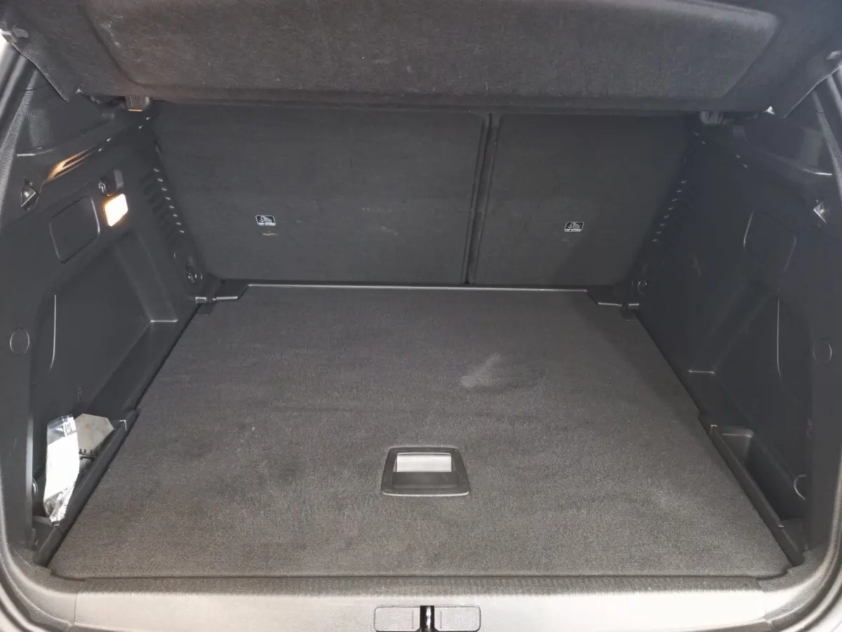 Coffre noir ouvert du Peugeot 3008 PureTech 130, vue de face montrant l'espace de chargement plat et les rangements latéraux.