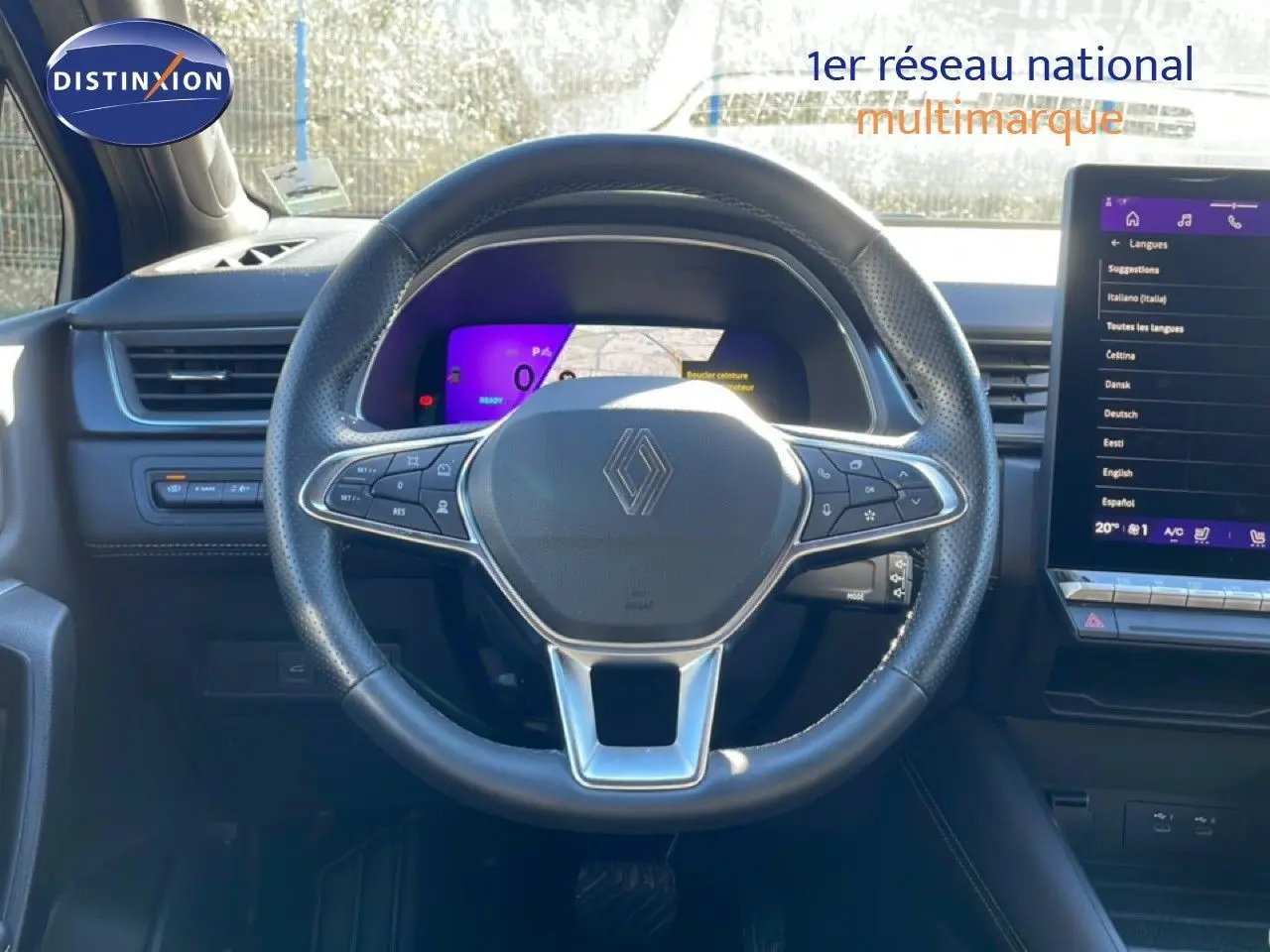 Vue intérieure centrée sur le volant noir perforé avec logo Renault, tableau de bord digital et écran tactile à droite.