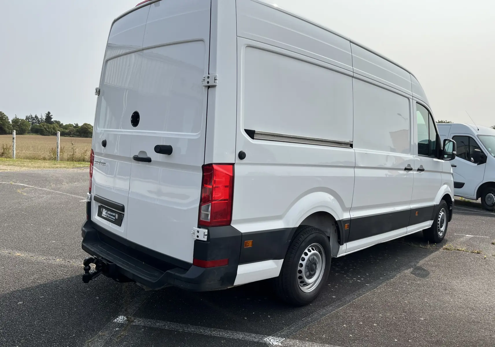 Volkswagen Crafter fourgon blanc vu en 3/4 arrière droit, avec attelage et panneaux latéraux lisses.