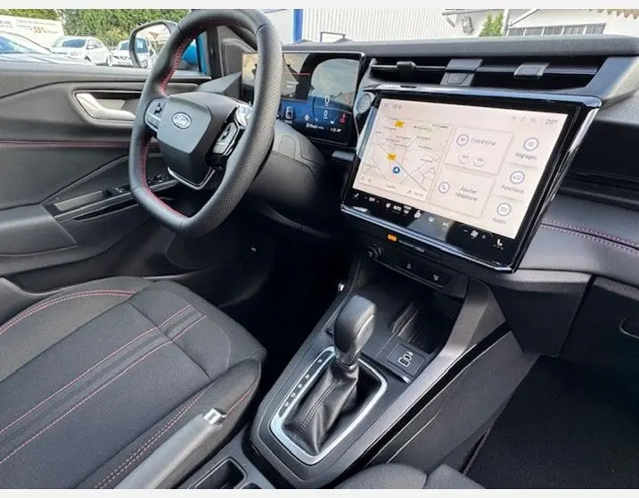 Vue intérieure côté conducteur du Ford Puma 2025 avec volant sport, surpiqûres rouges et écran tactile central.