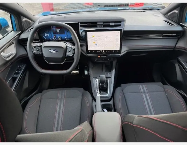 Vue intérieure avant du Ford Puma 2025, tableau de bord moderne avec écran tactile et sièges sport noirs à surpiqûres rouges.