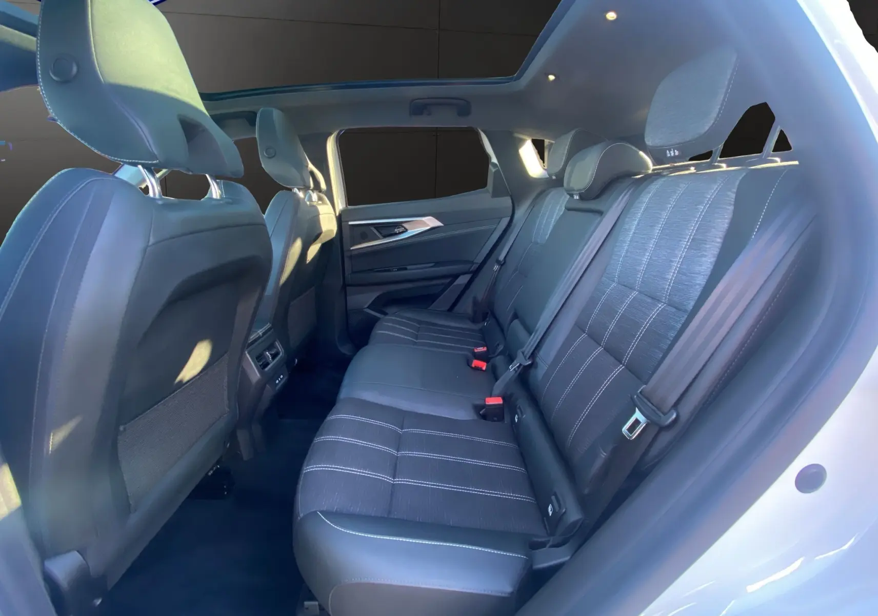 Vue intérieure arrière droite du Renault Austral blanc nacré, montrant les sièges noirs et le toit panoramique lumineux.