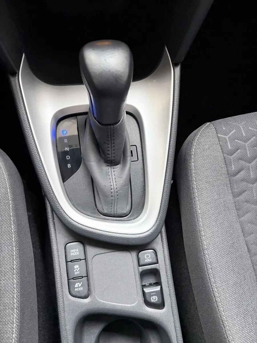 Gros plan sur la console centrale avec levier de vitesse automatique en cuir noir et boutons de mode de conduite, sièges gris.