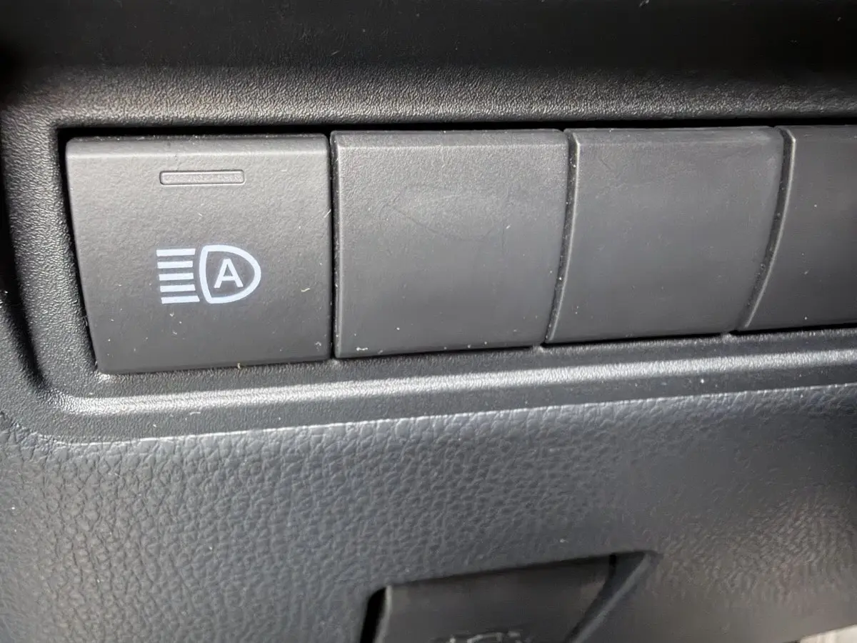 Gros plan sur le bouton de commande des feux automatiques dans l’habitacle noir de la Toyota Yaris Cross 2024 gris clair.