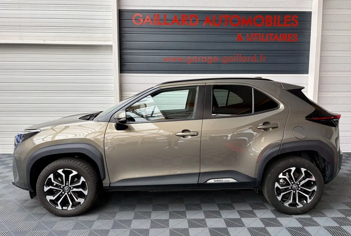 Profil droit de la Toyota Yaris Cross gris clair 2024 avec jantes alliage noires et logo Yaris Cross sur bas de caisse.