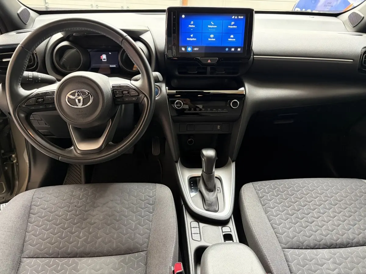 Vue intérieure avant centrée sur le volant cuir et l’écran tactile du tableau de bord de la Toyota Yaris Cross 2024.