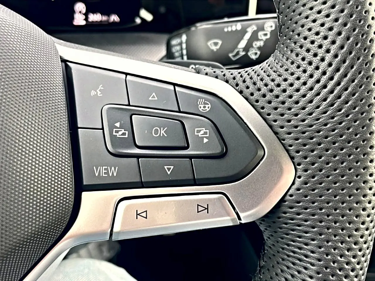 Gros plan sur les commandes multifonctions gauche du volant perforé noir de la Volkswagen Golf 2026.
