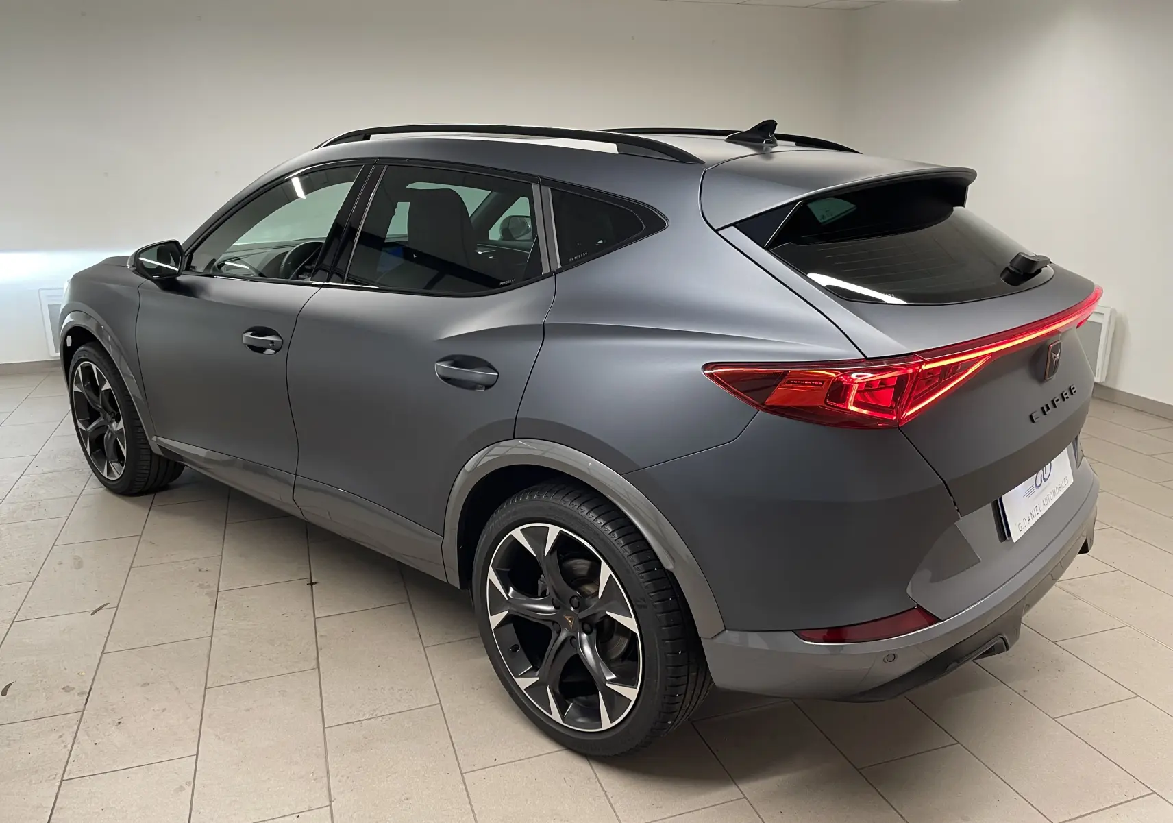 Vue 3/4 arrière droite du CUPRA Formentor 1.5 TSI 150 DSG7 en gris magnétique mat avec feux arrière allumés.