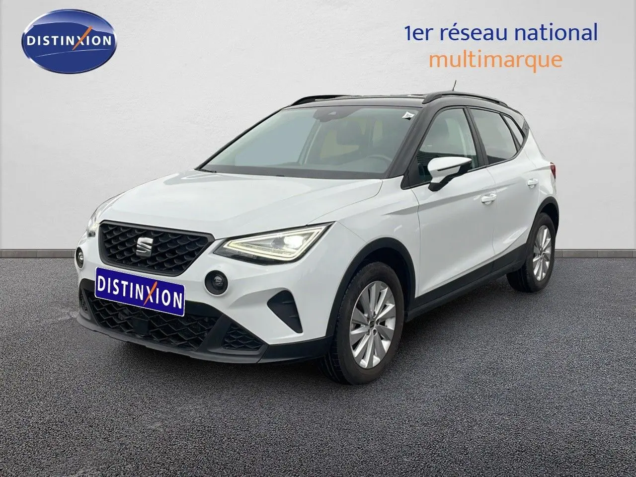 SEAT Arona blanc alpin métal avec toit noir, vue 3/4 avant droit, sur sol gris devant un mur blanc.