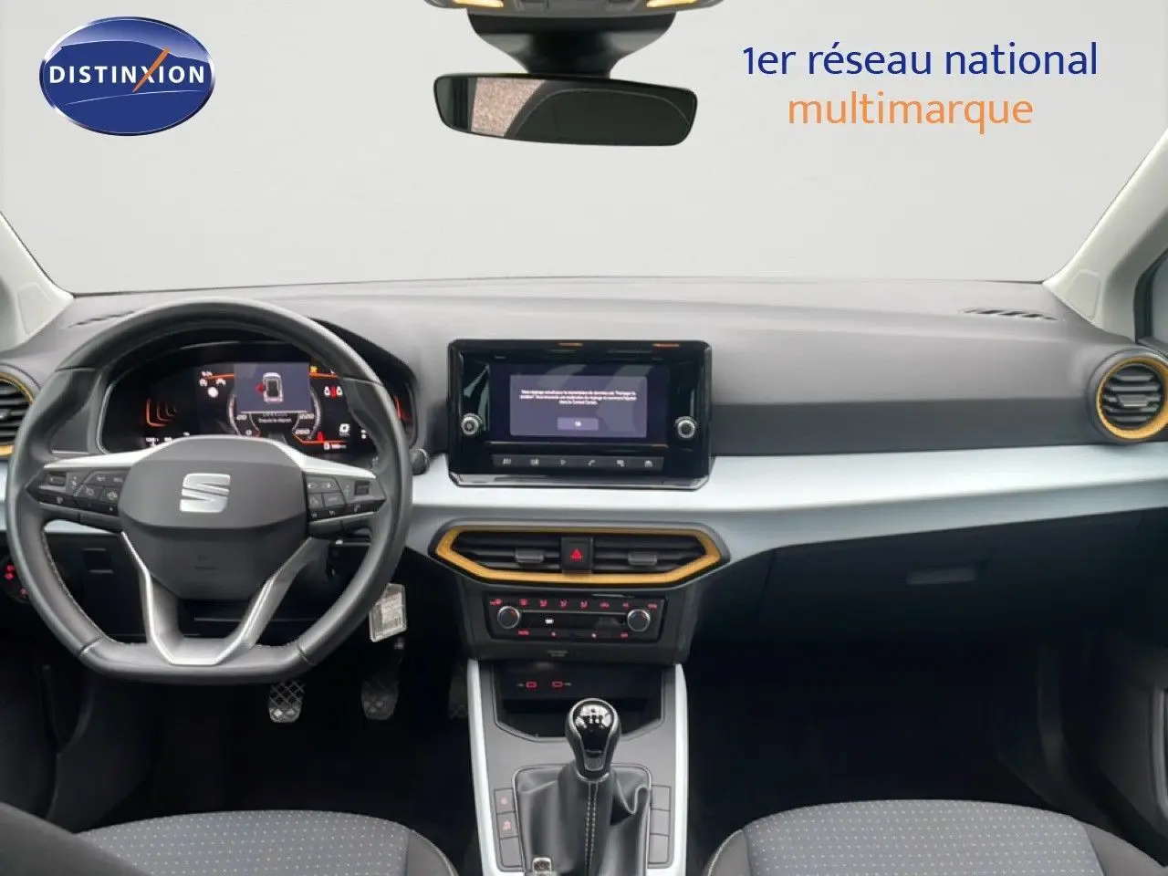 Vue intérieure avant du tableau de bord du SEAT Arona blanc alpin métal, avec volant cuir et touches jaunes autour des aérateurs.