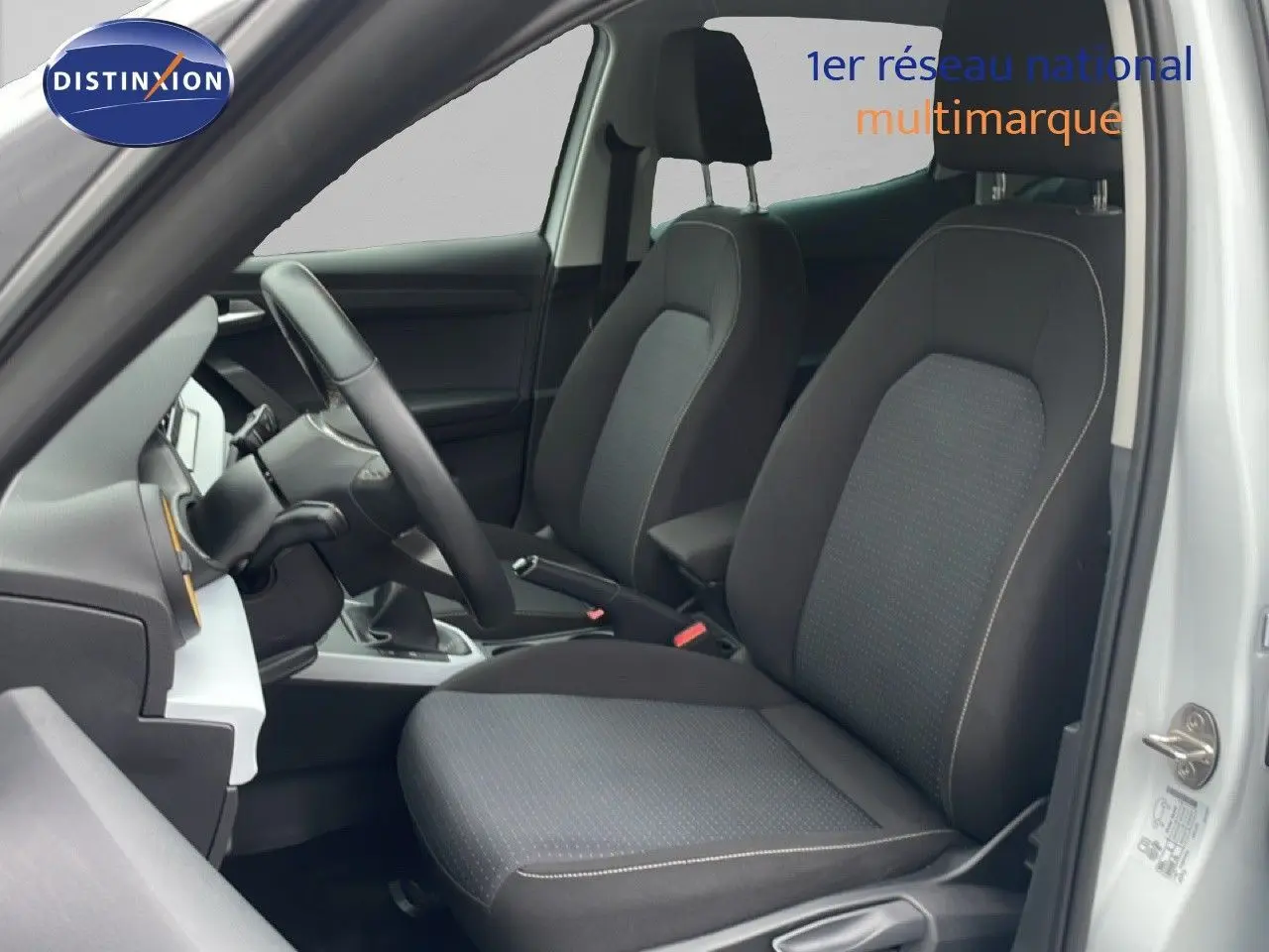 Vue intérieure côté conducteur du SEAT Arona 2025 blanc alpin, montrant les sièges avant en tissu noir et volant multifonction.