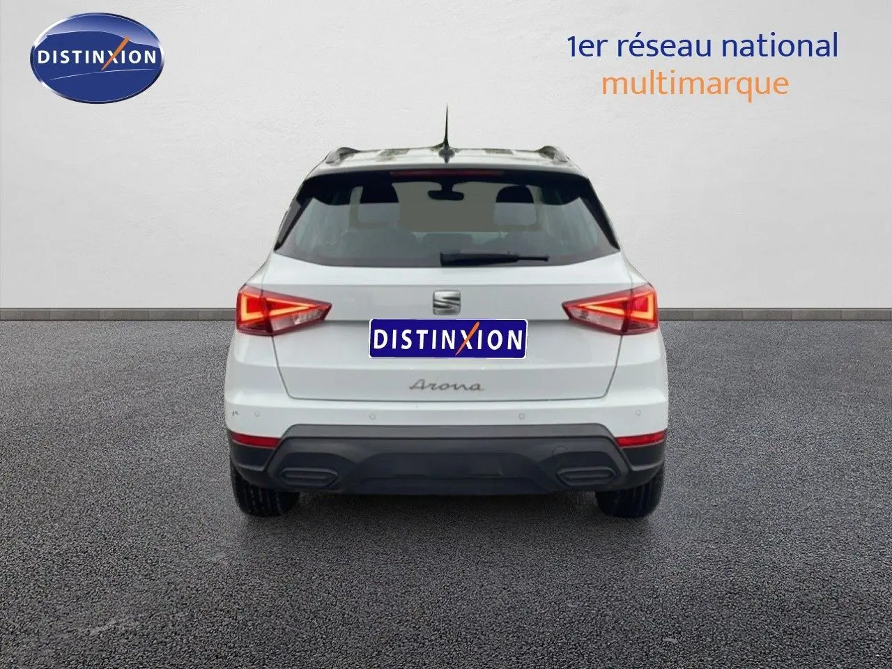 Vue arrière d’un SEAT Arona blanc alpin avec toit noir, feux arrière allumés sur fond neutre.