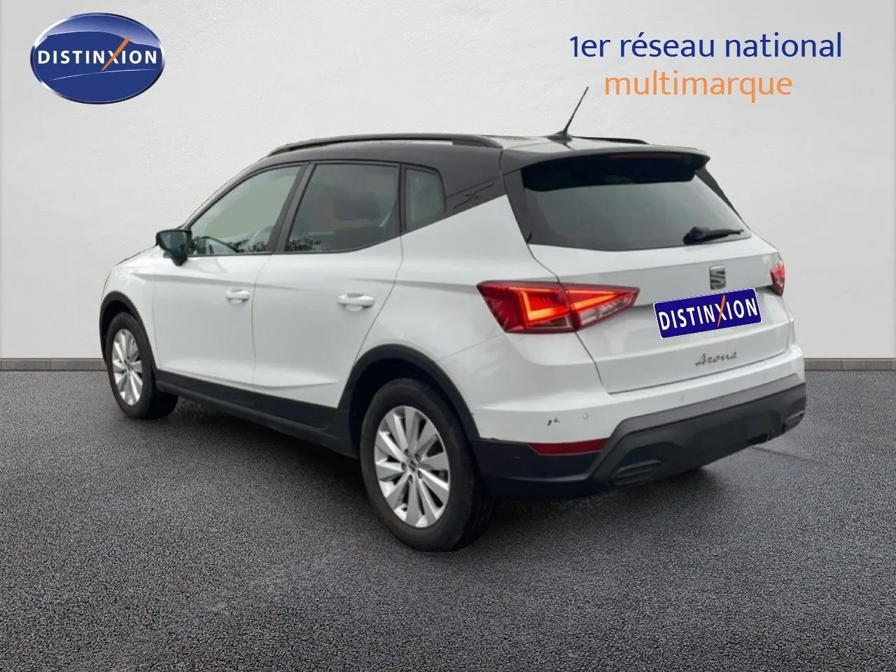 SEAT Arona blanc alpin métal avec toit noir, vue 3/4 arrière côté gauche, feux arrière allumés.