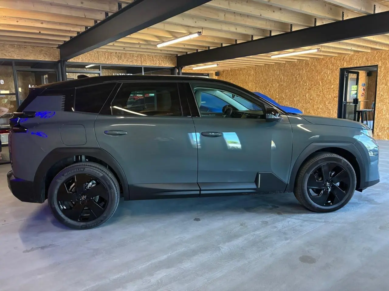 Profil droit du Citroën C5 Aircross II vert avec toit noir et jantes noires dans un garage intérieur.