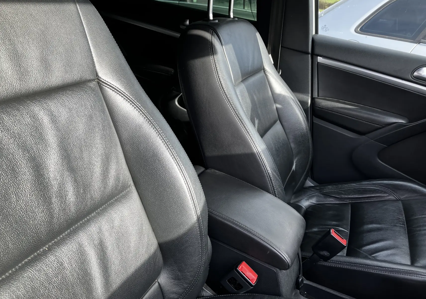 Gros plan sur les sièges avant en cuir noir du Volkswagen Tiguan blanc, version 2013, avec accoudoir central visible.