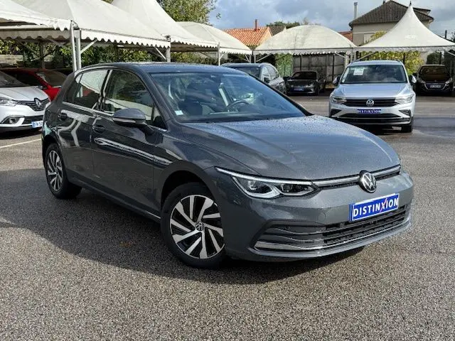 Volkswagen Golf VIII 1.4 e-Hybrid gris dauphin vue 3/4 avant sur parking avec logo Distinxion visible