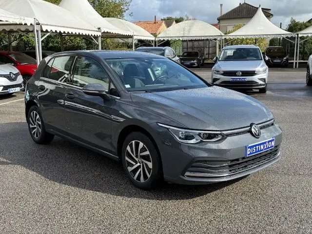 Volkswagen Golf VIII 1.4 e-Hybrid gris dauphin vue 3/4 avant droit sur parking sous un ciel partiellement nuageux