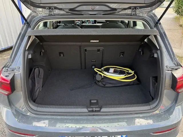 Coffre ouvert d'une Volkswagen Golf VIII gris dauphin, vue arrière, avec câble de recharge hybride visible à l'intérieur.