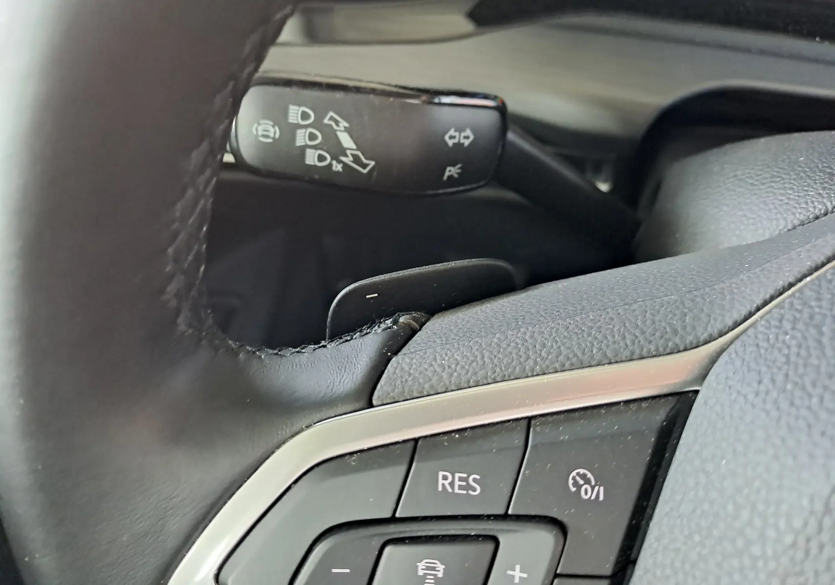 Gros plan sur les commandes au volant en cuir noir de la Volkswagen Golf VIII hybride rechargeable, avec régulateur de vitesse.