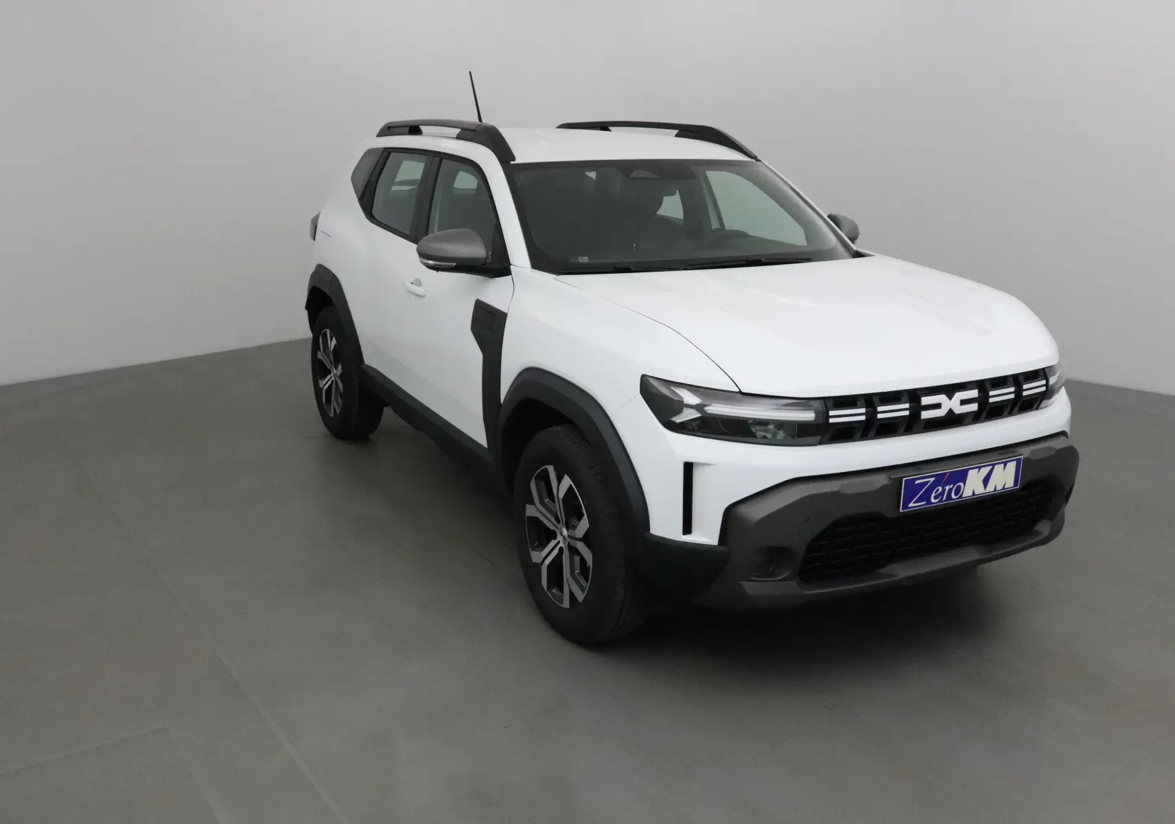Dacia Duster 2025 blanc glacier en 3/4 avant droit, avec calandre noire et jantes alliage 17 pouces.
