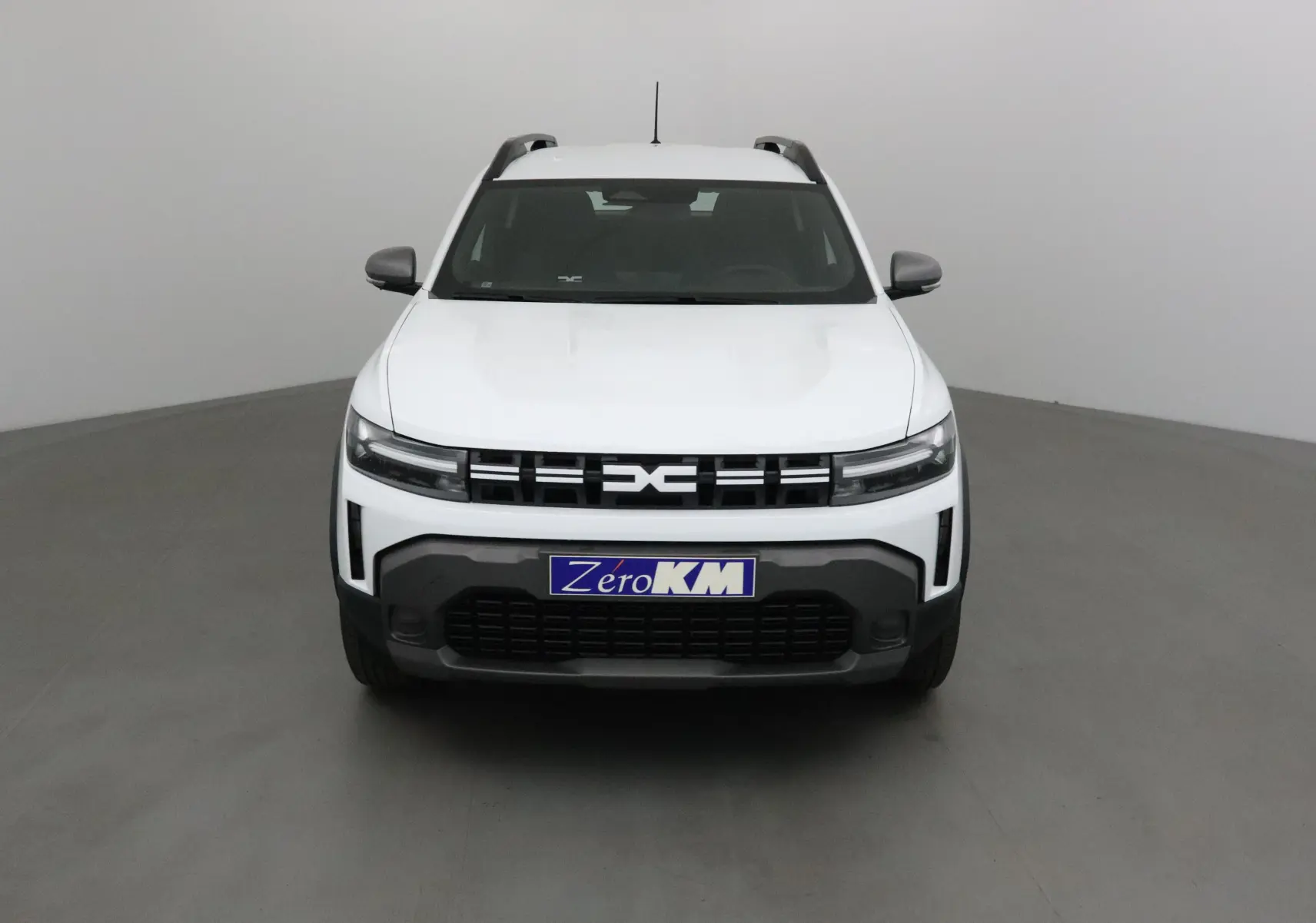 Vue frontale d'un Dacia Duster blanc glacier 2025 avec calandre noire et logo central distinctif.