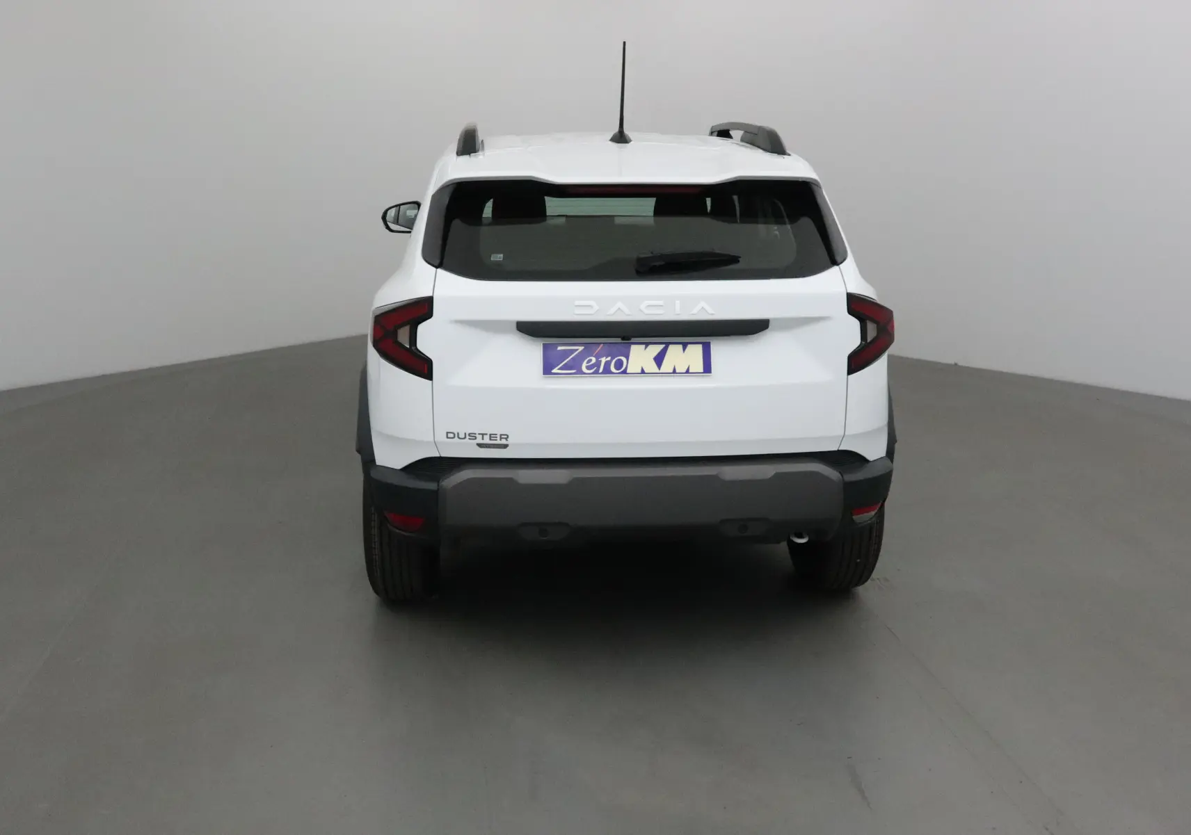 Vue arrière du Dacia Duster blanc glacier 2025, mettant en valeur ses feux arrière en forme de C et son pare-chocs noir robuste.