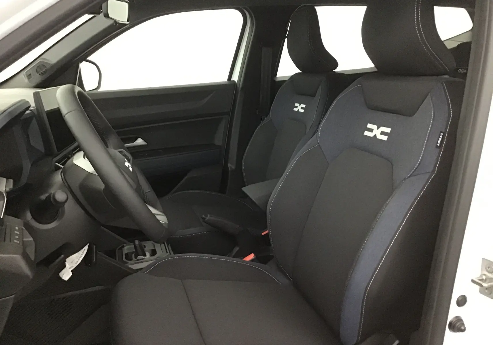 Vue intérieure côté conducteur du Dacia Duster 2025 blanc glacier, sièges avant noirs avec logo distinctif brodé.