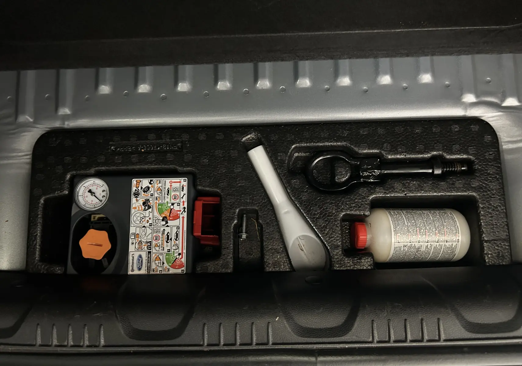 Gros plan sur le kit de réparation pneumatique dans le coffre d'un Ford EcoSport gris 2018, version Titanium.