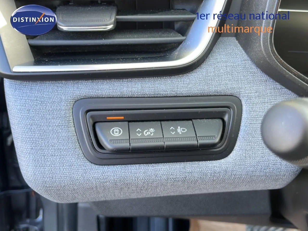 Gros plan sur les commandes d'éclairage intégrées dans la garniture tissu gris clair du tableau de bord de la Renault Clio 2025.