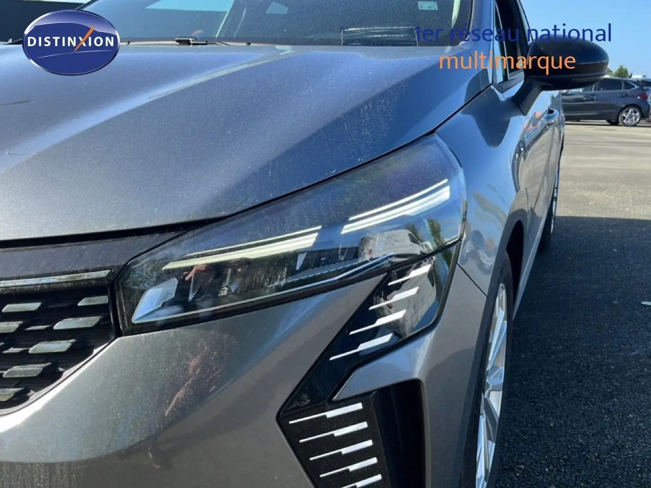 Gros plan sur l'avant droit de la Renault Clio gris schiste métal, mettant en valeur son phare LED et la calandre moderne.