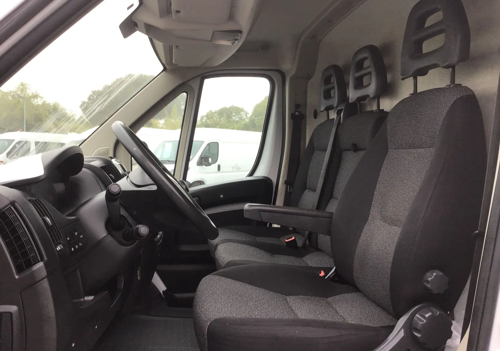 Vue intérieure côté conducteur du Fiat Ducato Fourgon blanc 2021, montrant les sièges avant en tissu gris et noir.
