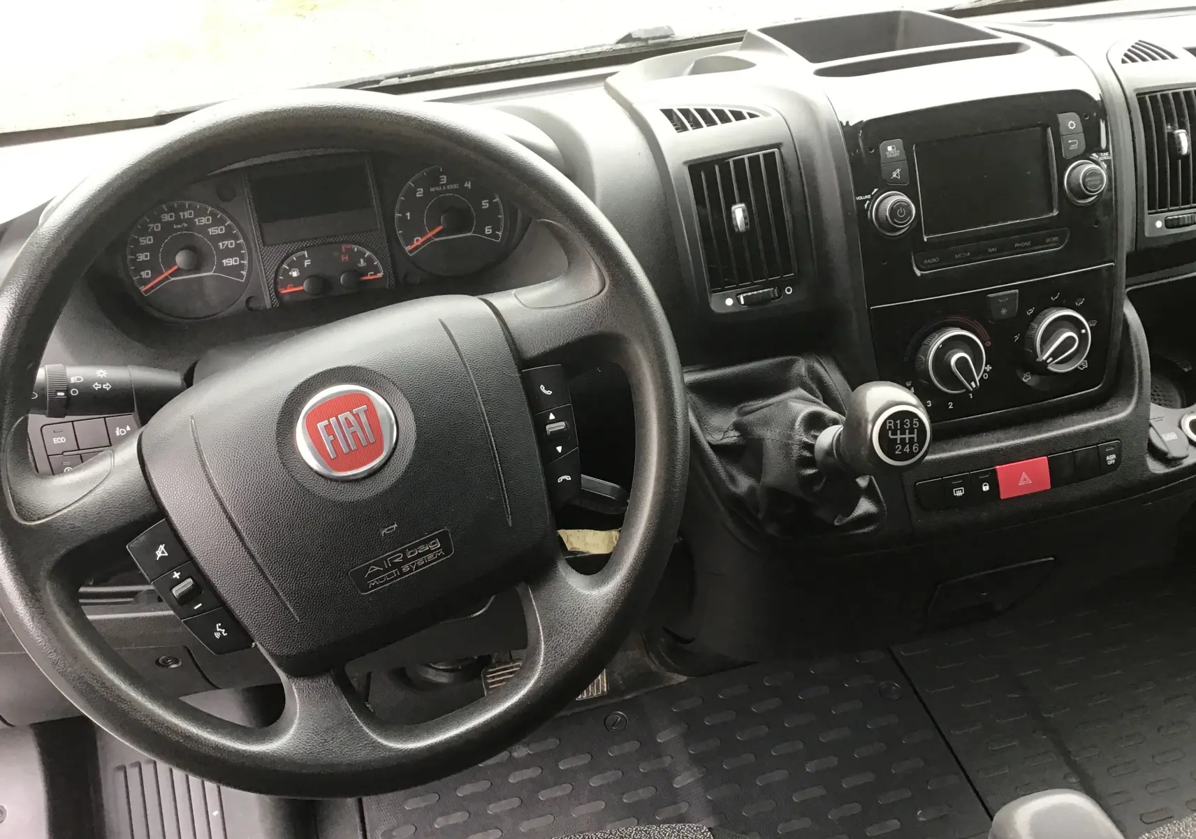 Vue intérieure du tableau de bord du Fiat Ducato Fourgon 2021, volant noir avec logo rouge et levier de vitesse manuel.