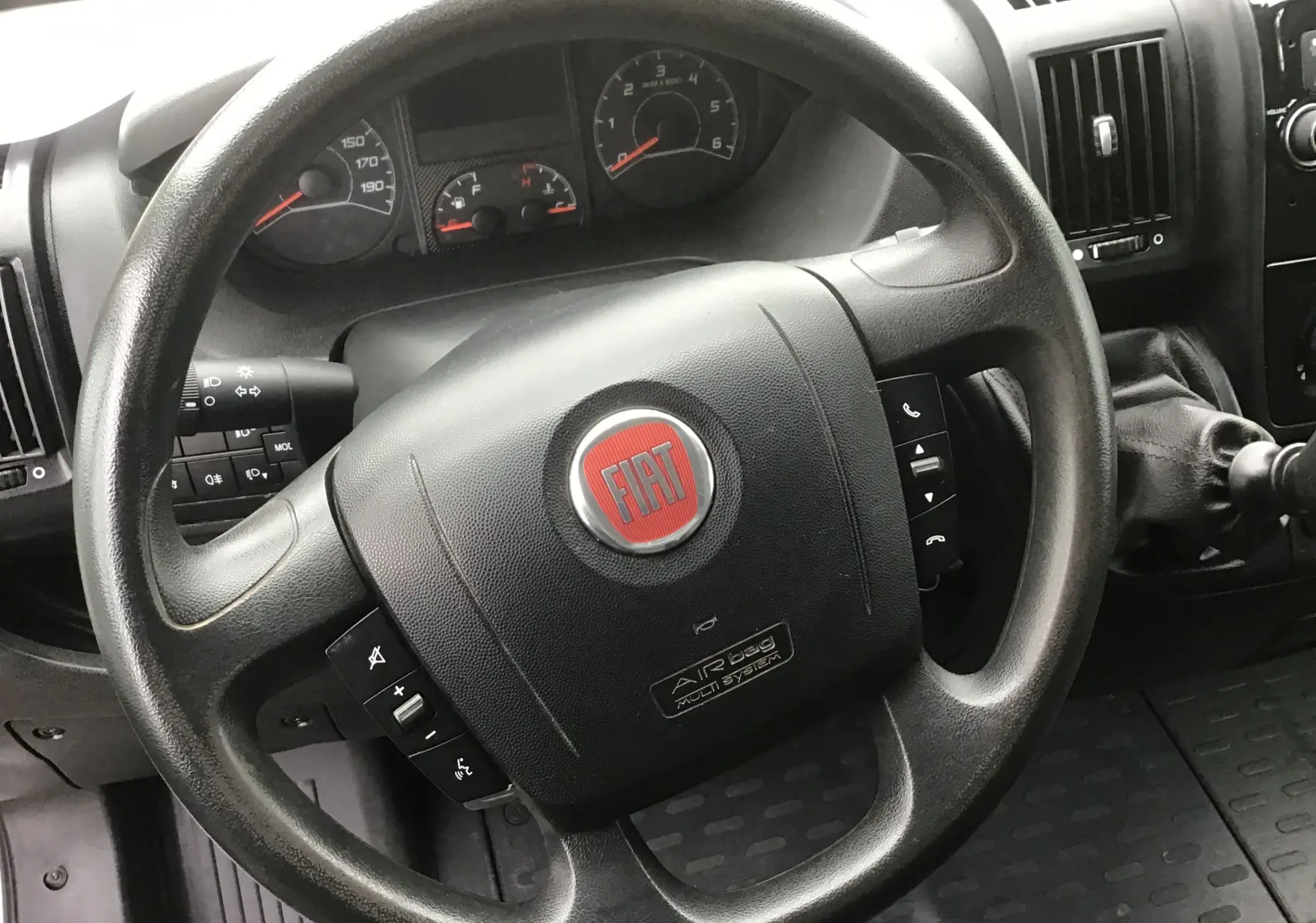 Vue intérieure centrée sur le volant noir du Fiat Ducato Fourgon blanc, avec commandes intégrées visibles sur le volant.