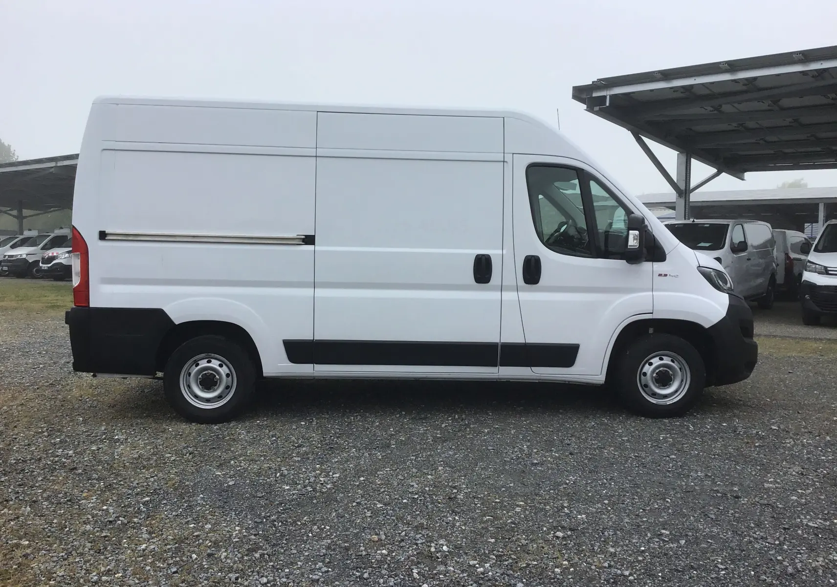 Fiat Ducato Fourgon blanc vu de profil côté droit, avec porte coulissante et protections noires sur bas de caisse.