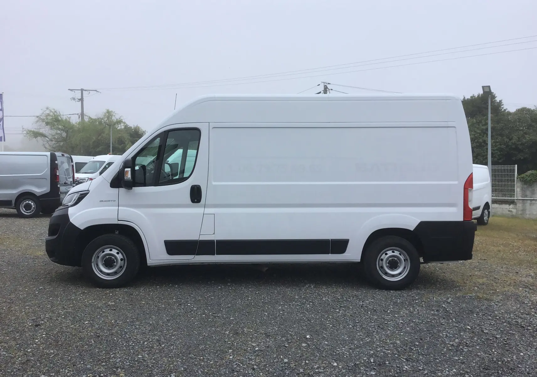 Fourgon blanc FIAT Ducato 35 MH2 vu de profil côté gauche sur un sol gravillonné, sans marquage visible.