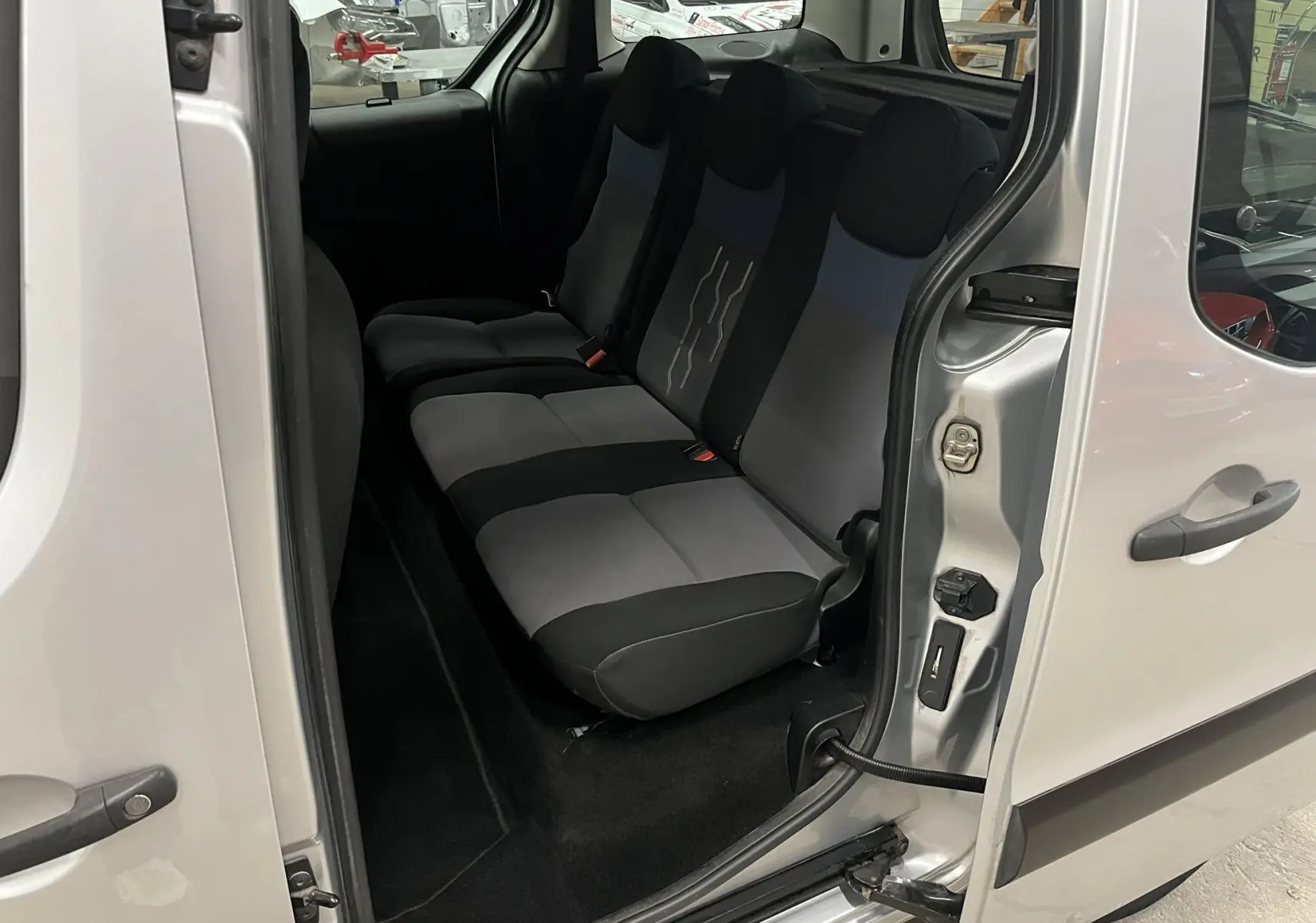 Vue intérieure côté droit sur la banquette arrière grise et noire du Peugeot Partner Tepee gris aluminium avec porte coulissante ouverte.
