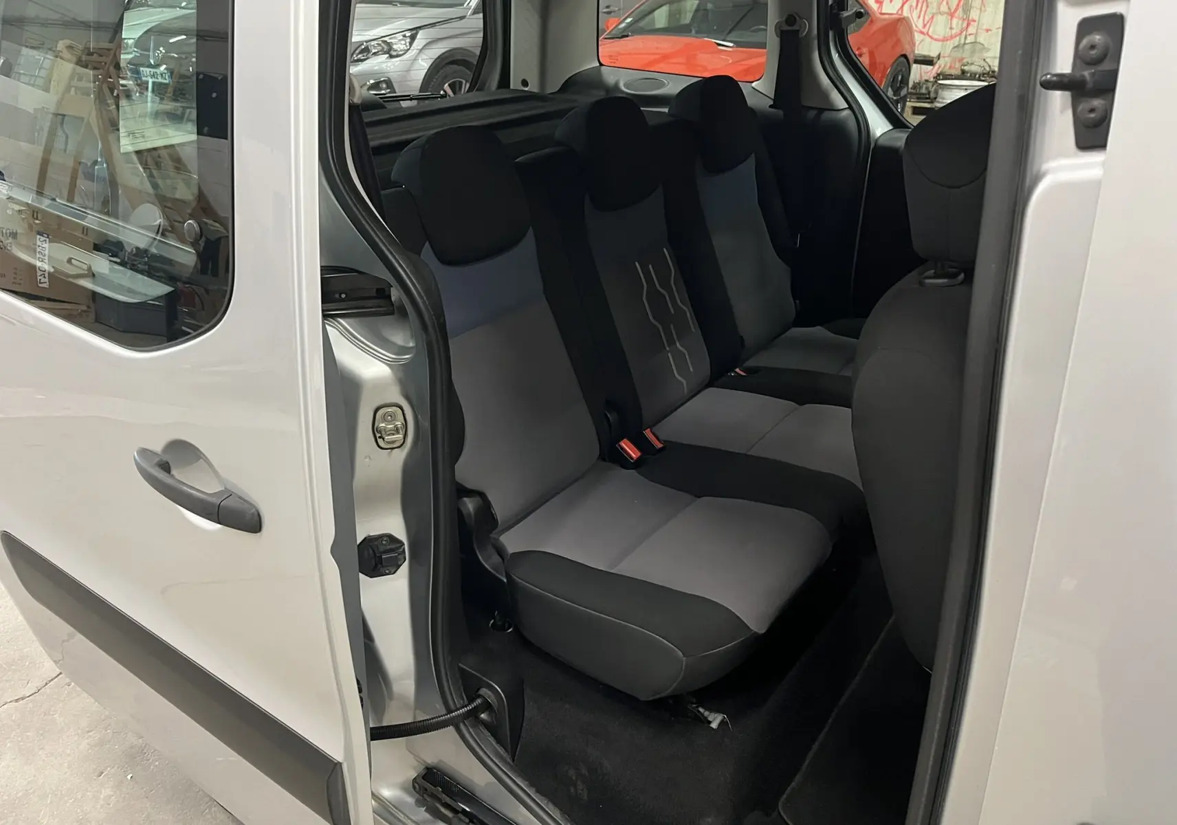 Vue intérieure côté gauche sur les sièges arrière gris et noirs du Peugeot Partner Tepee gris aluminium avec porte coulissante ouverte.