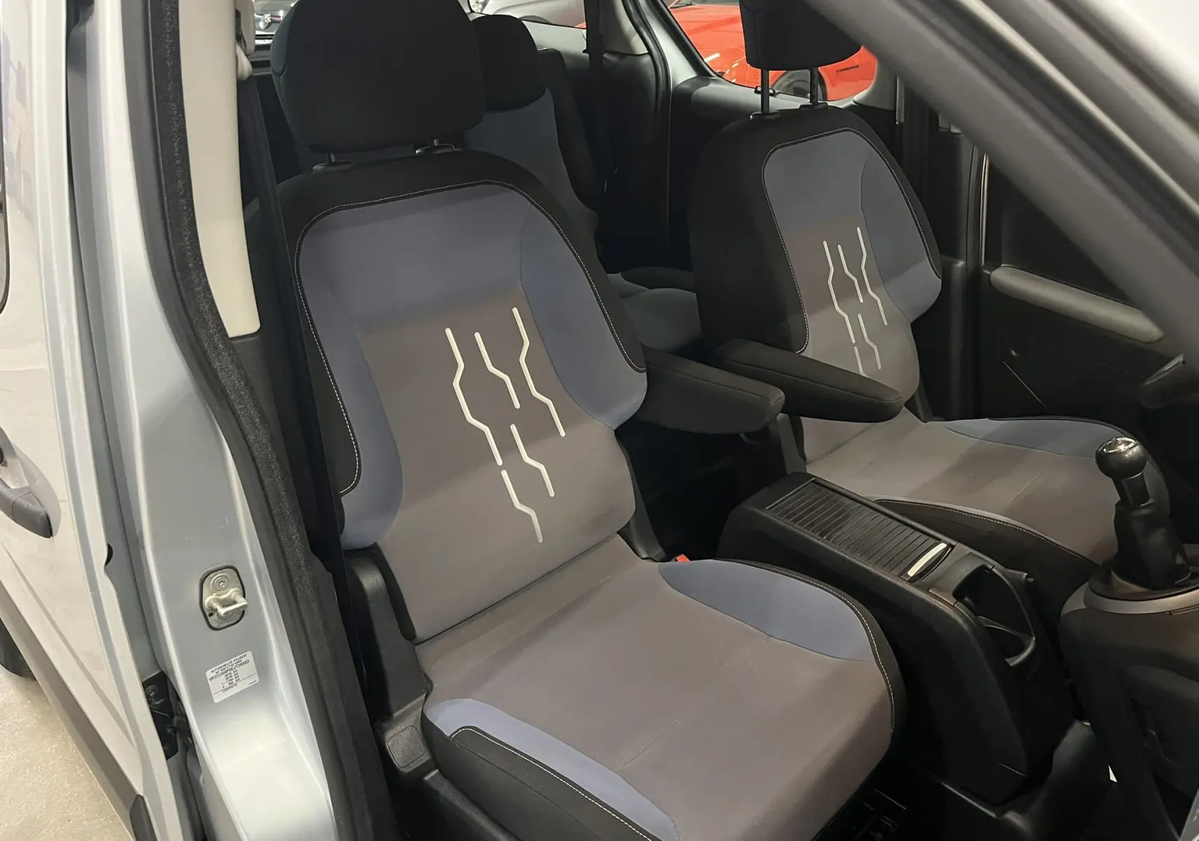 Vue intérieure côté conducteur du Peugeot Partner Tepee gris aluminium 2013, sièges tissu gris et bleu avec motifs blancs.