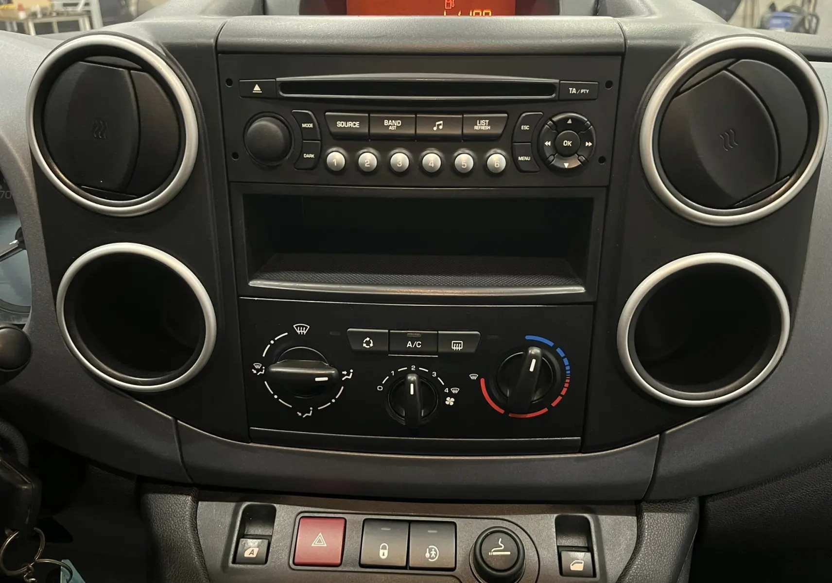 Vue rapprochée du tableau de bord noir du Peugeot Partner Tepee 2013 avec commandes de climatisation et radio intégrée.