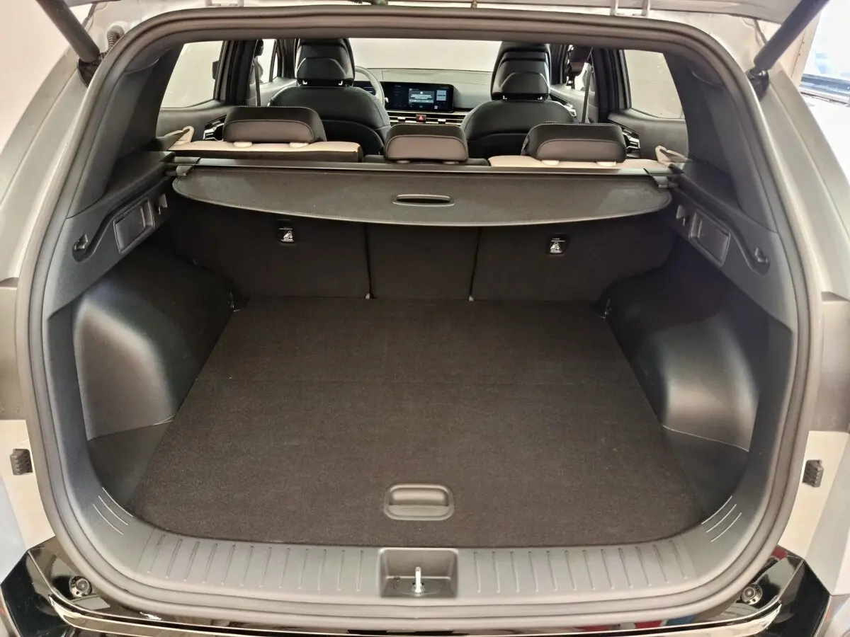 Coffre ouvert du KIA Sportage gris clair, vue arrière montrant l’espace de chargement et la plage arrière rétractable.