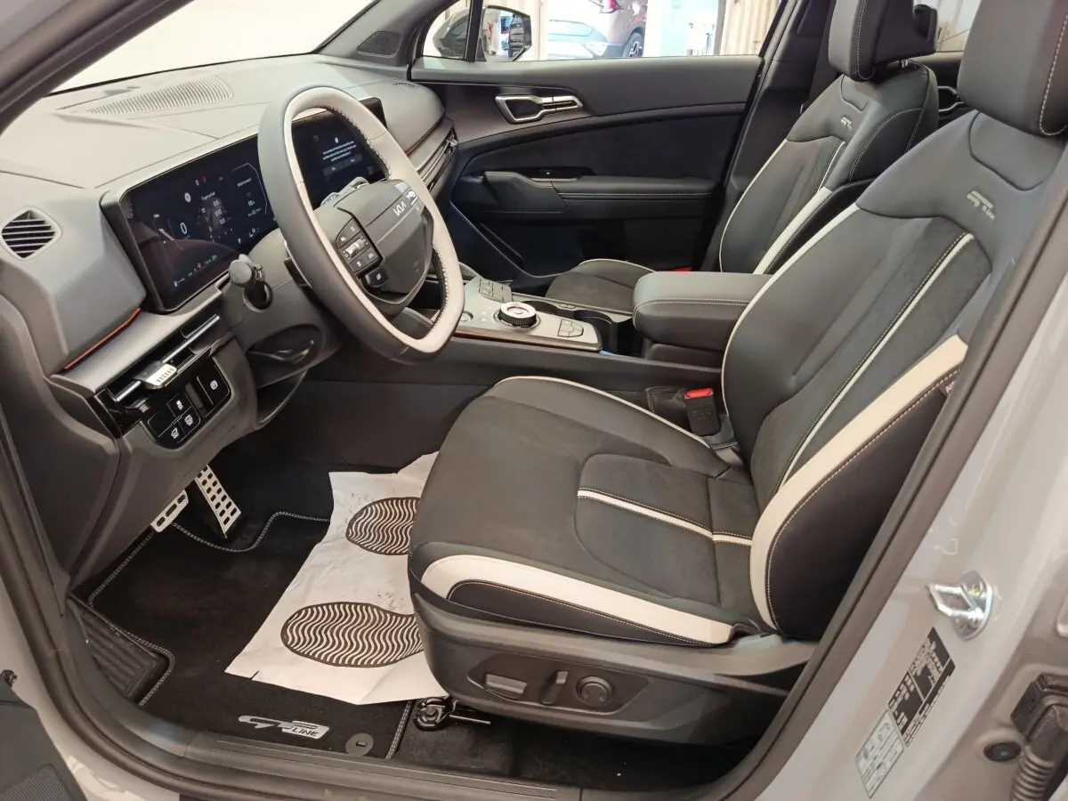 Intérieur avant droit du Kia Sportage gris clair 2026, sièges GT-Line noirs avec surpiqûres blanches et tableau de bord numérique.