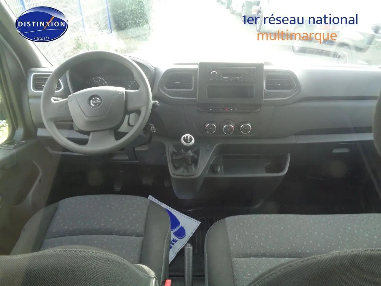 Intérieur de l'Opel Movano Fourgon 2022, vue frontale du tableau de bord avec volant, levier de vitesse manuel et sièges gris.