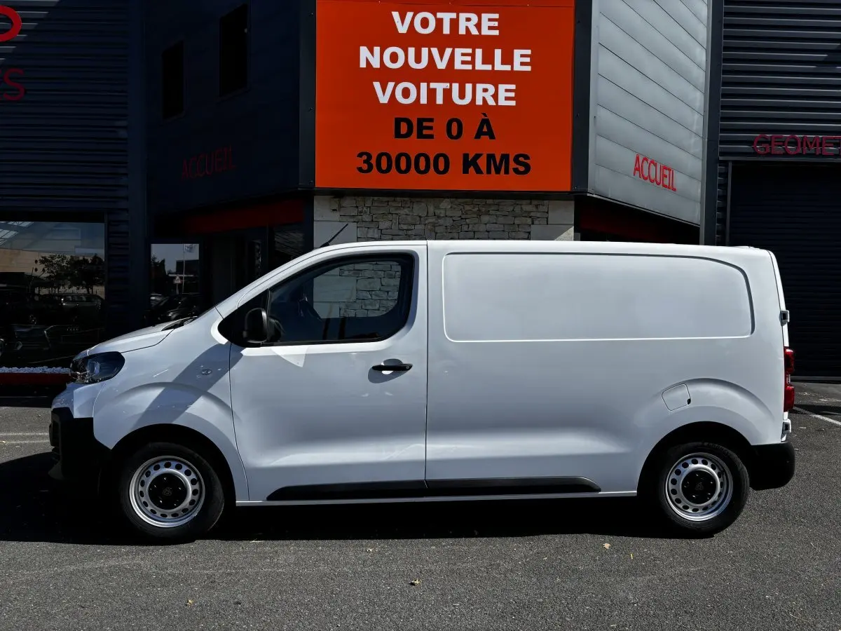 Profil côté gauche d'un Peugeot Expert Fourgon blanc 2025 garé devant un bâtiment avec panneau orange visible.