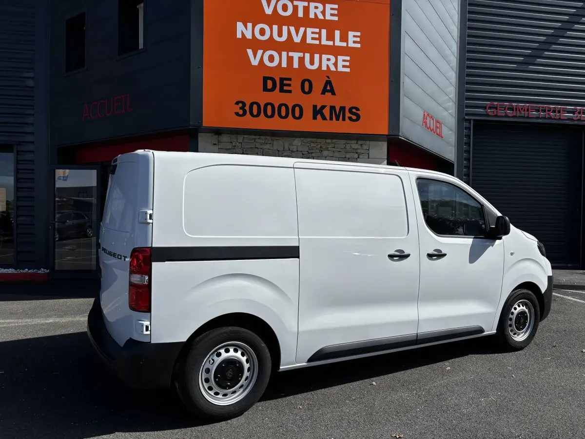 Peugeot Expert Fourgon blanc vu de profil côté droit, stationné devant un bâtiment commercial avec panneau orange.