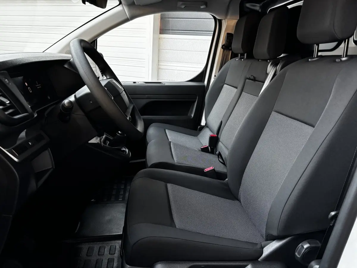 Vue intérieure côté conducteur du Peugeot Expert Fourgon blanc 2025, montrant les sièges avant en tissu gris et noir.