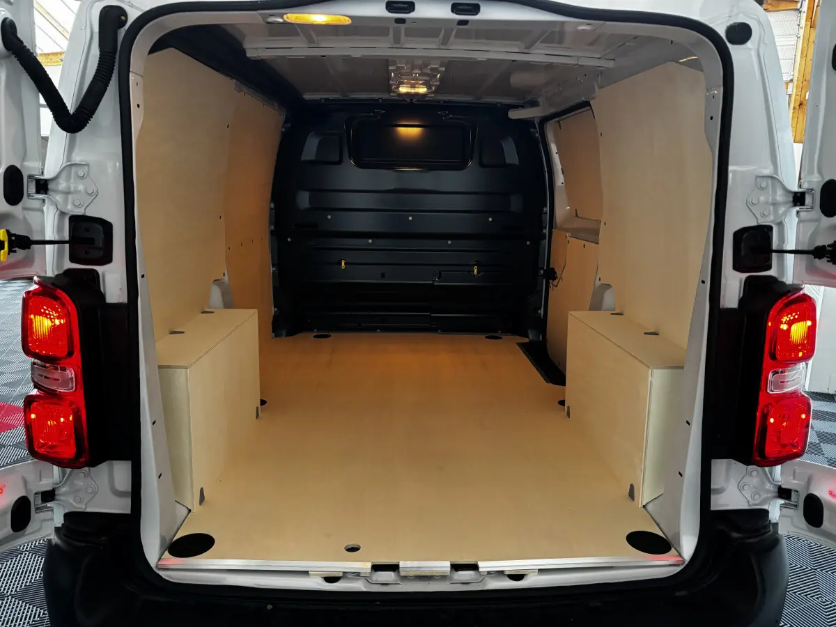 Intérieur du coffre blanc Peugeot Expert Fourgon Taille M 2025, vue arrière ouverte avec plancher et parois en bois clair.