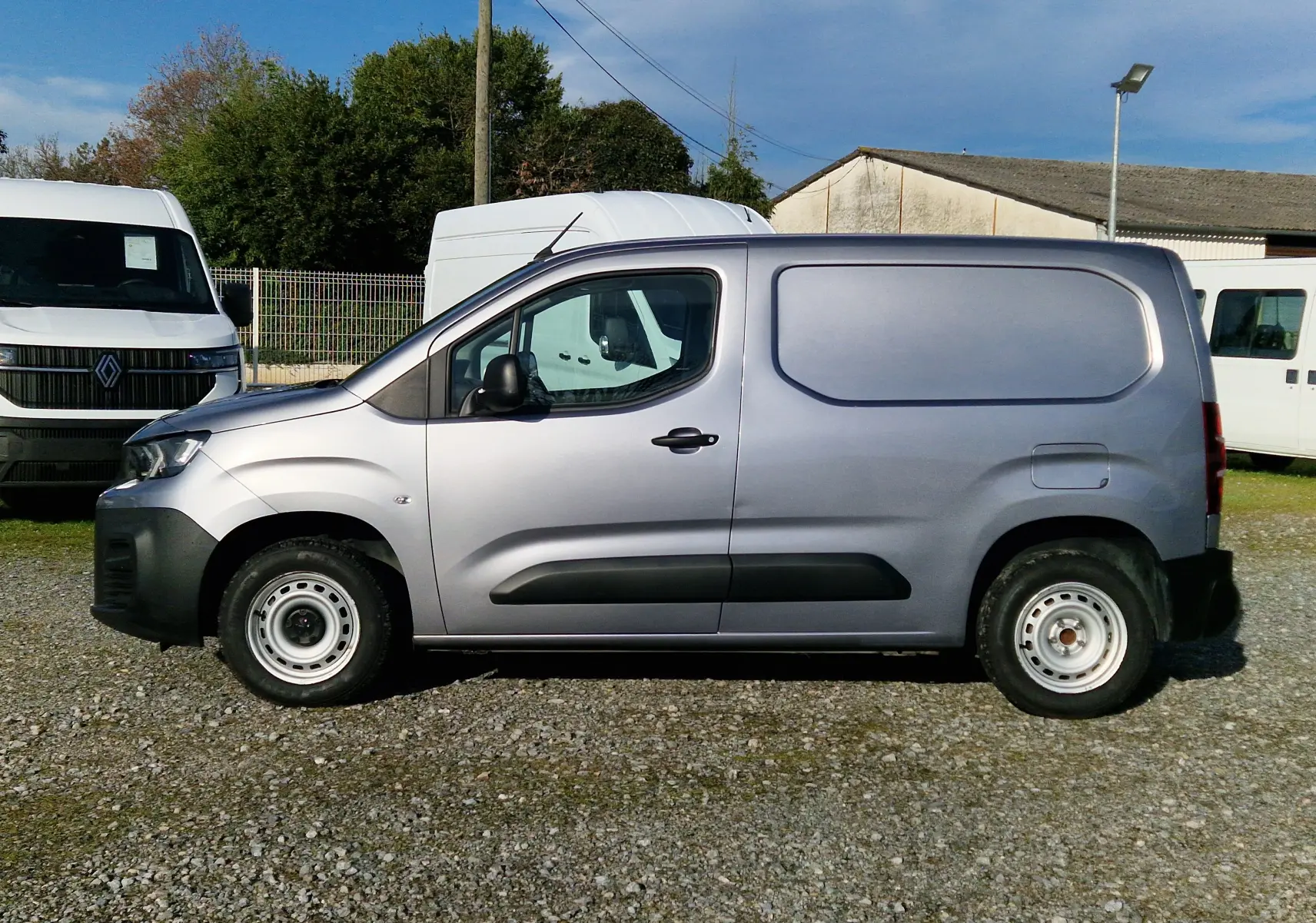 Vue de profil côté gauche d'un Peugeot Partner gris Artense utilitaire avec porte latérale pleine, stationné sur un sol gravillonné.