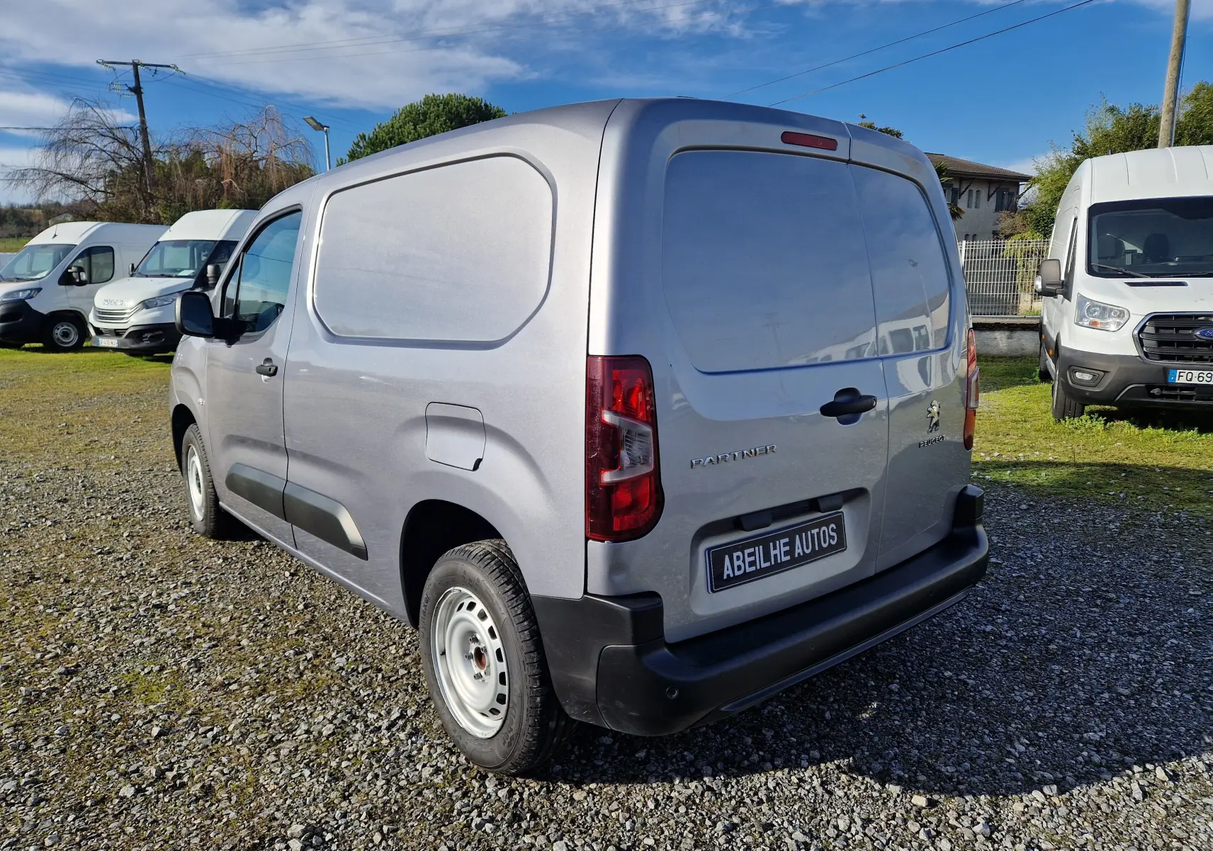 Peugeot Partner gris Artense vu en 3/4 arrière droit sur un parking, avec plaque Abeilhe Autos visible.