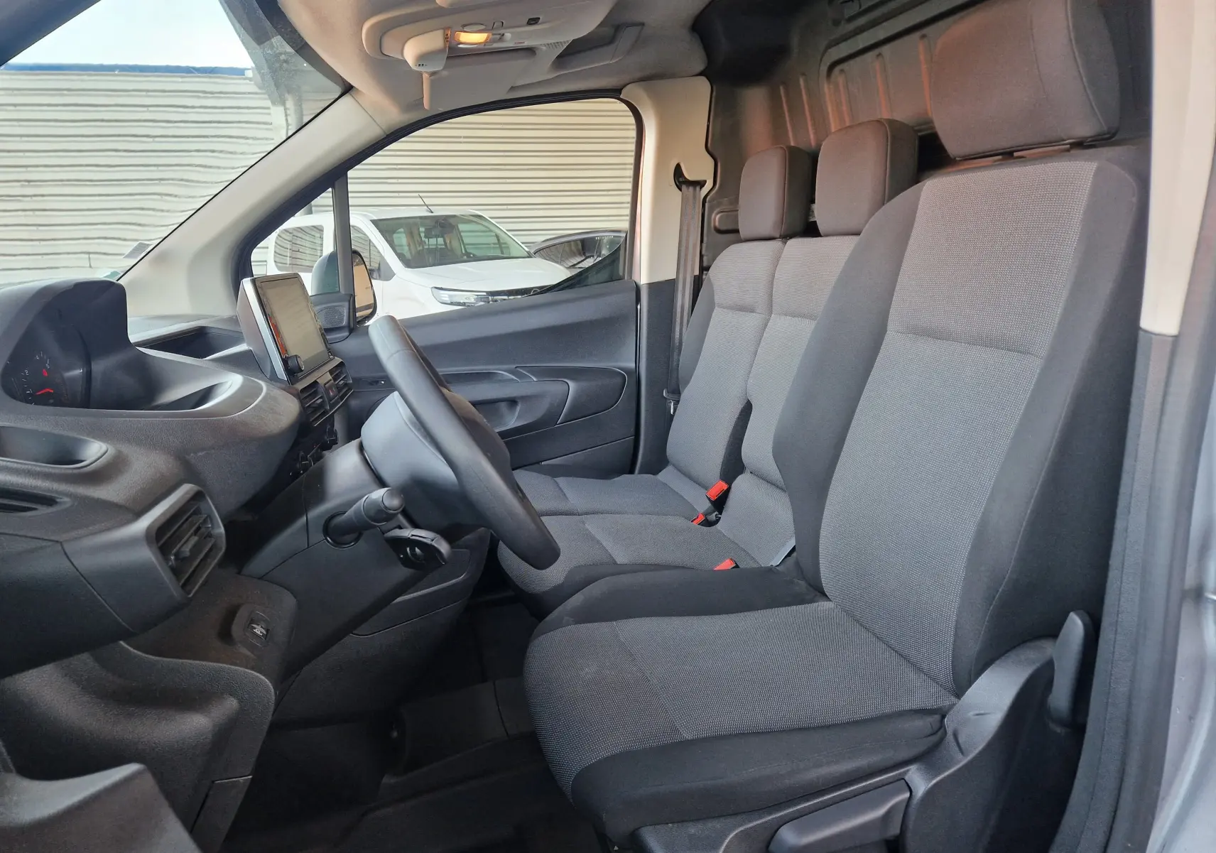 Intérieur du Peugeot Partner gris Artense 2021 vu côté conducteur, montrant les sièges avant et le tableau de bord.