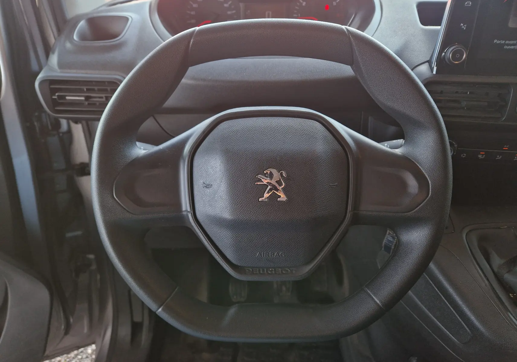 Gros plan sur le volant noir du Peugeot Partner 2021, avec logo lion au centre et tableau de bord en arrière-plan.